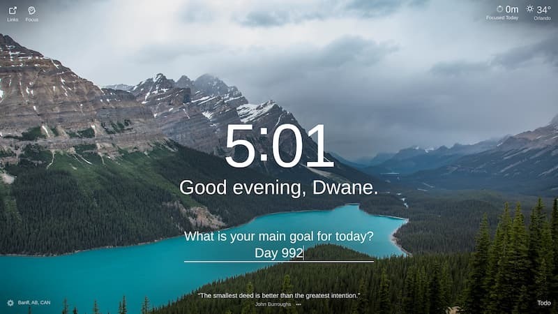 A panoramic view of a lake in the Rocky Mountains, with a steep mountainside on the right and a smaller mountainside on the left. The lake is a vivid, almost iridescent blue. Green pines and fir trees are silhouetted against the water and snow-capped peaks. The location is Banff National Park, Canada.