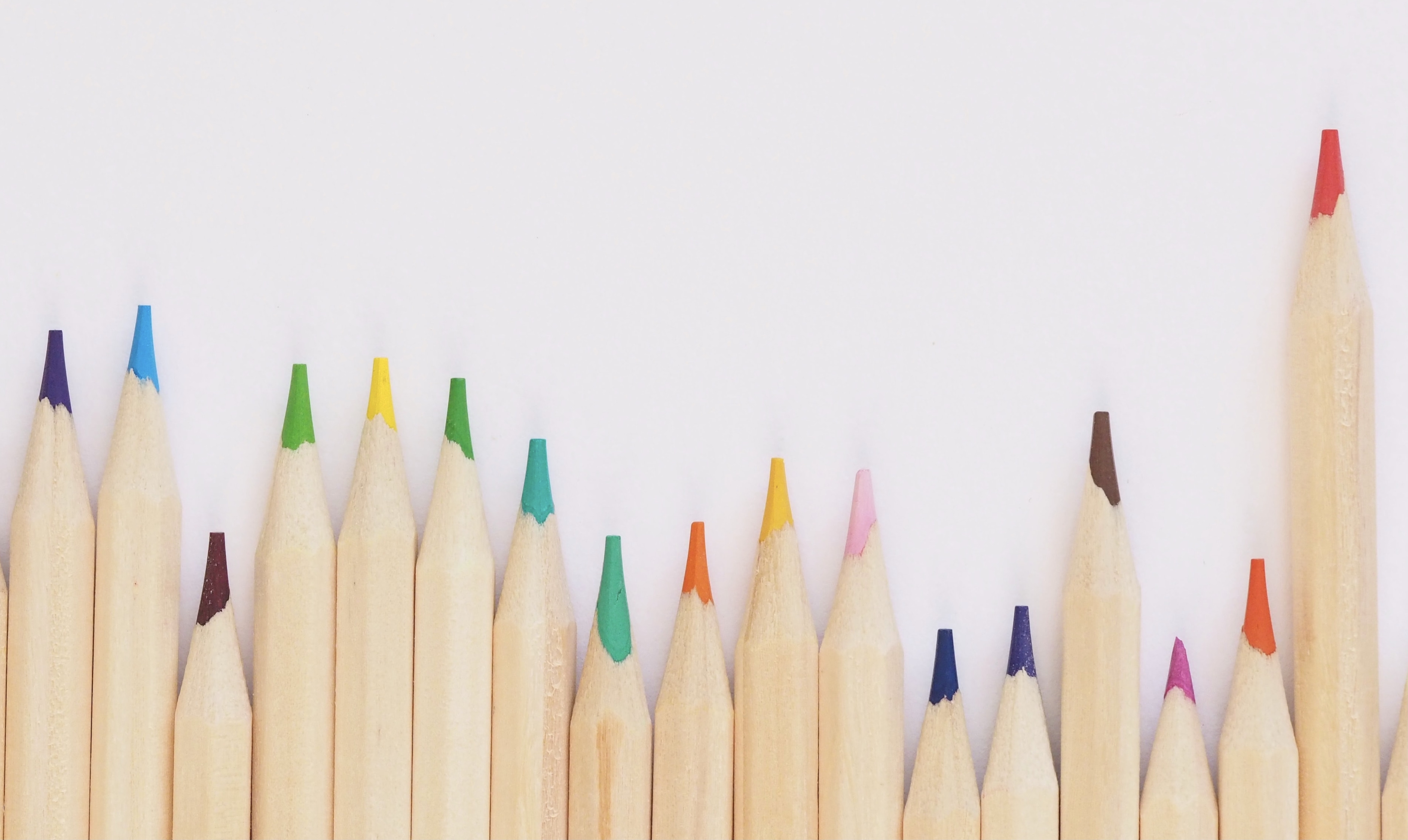 Multicolored pencils are laying flat on a light background. The pencils are not aligned, with some of them appearing to be longer than others.