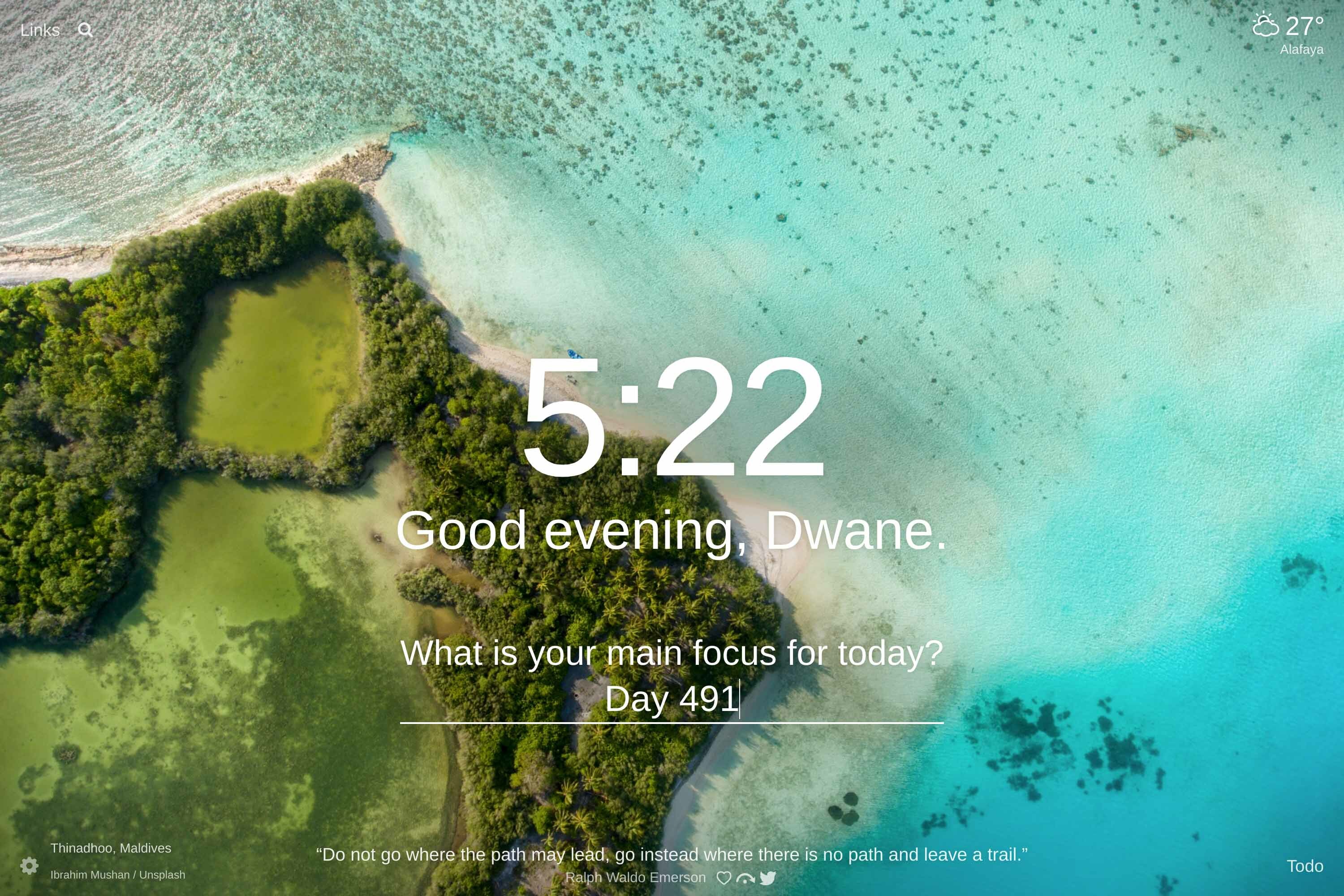 Overhead shot of an island in Thinadhoo, Maldives with the ocean surrounding a strip of land with a green lagoon in the center.