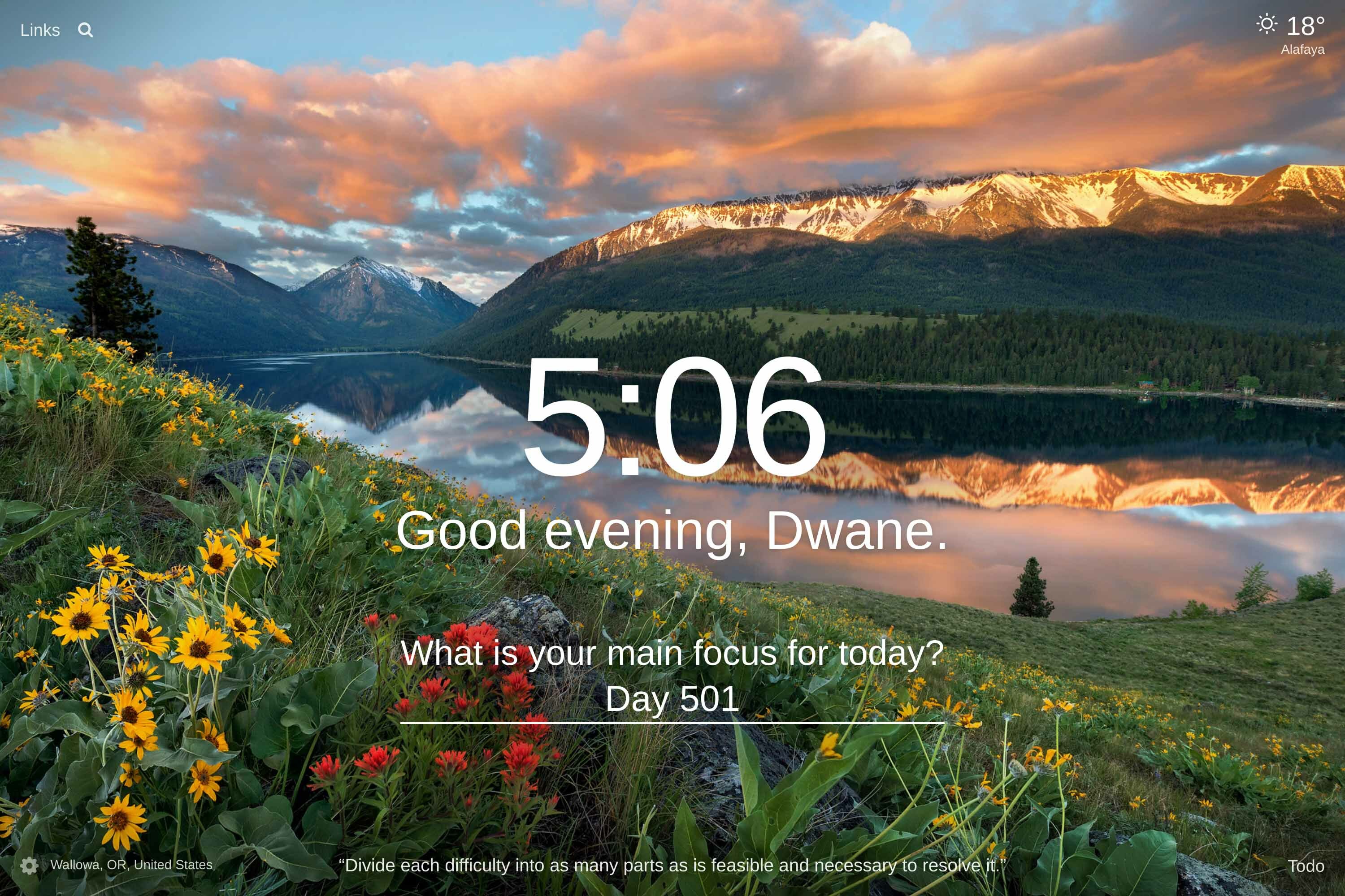A field filled with tall green grass and red and yellow flowers with a lake and a mountain range in the distance at sunset in Wallowa, OR, United States