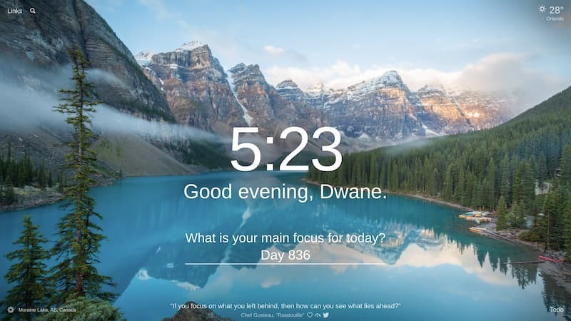 Moraine Lake in AB, Canada with blue water that reflects the tall, stone, snow topped mountain chain on the left and on the right, a pine tree forest with some boats in a dock on the show.